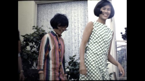 Two teenage girls from the Jung family walk past camera smiling, wearing colorful stripped and checkered outfits (late 50's early 60's style).
